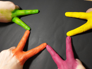 Dedos de personas pintados de colores formando una estrella a la que le falta una punta.