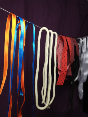hilos, trazos de telas y cordones de diferentes colores y texturas colgando de un hilo que los atraviesa