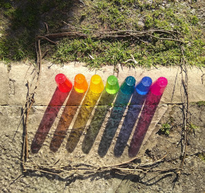 vasos de colores en el piso siendo atravesados por la luz del sol, formando un arcoíris en el piso.