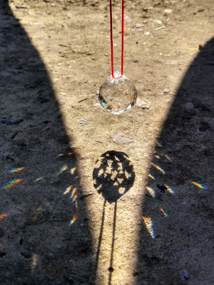 una piedrita de cristal siendo atravesada por los rayos del sol, formando pequeños arcoíris en el suelo